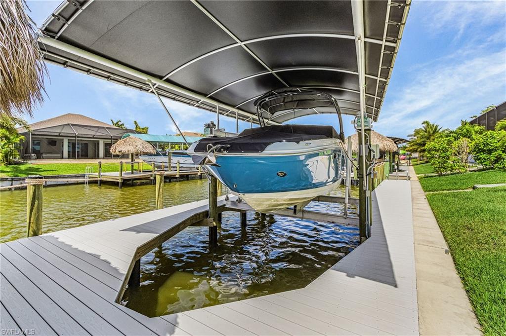 Waterfront property featuring a private boat lift with a canopy, composite decking, and a grass tiki hut