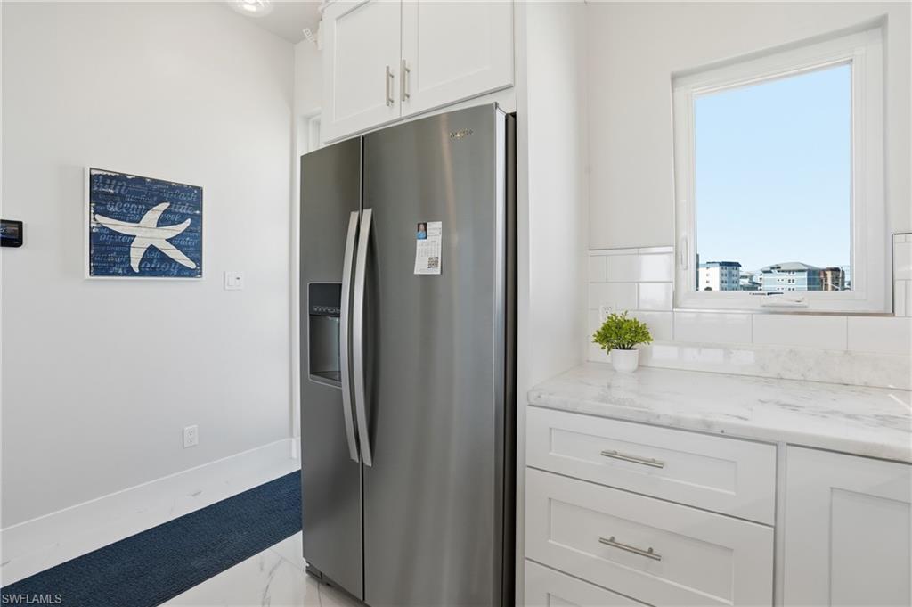 Kitchen featuring stainless steel fridge, white cabinets, light stone counters, light marble finish floors, and tasteful backsplash - Virtually Edited Image