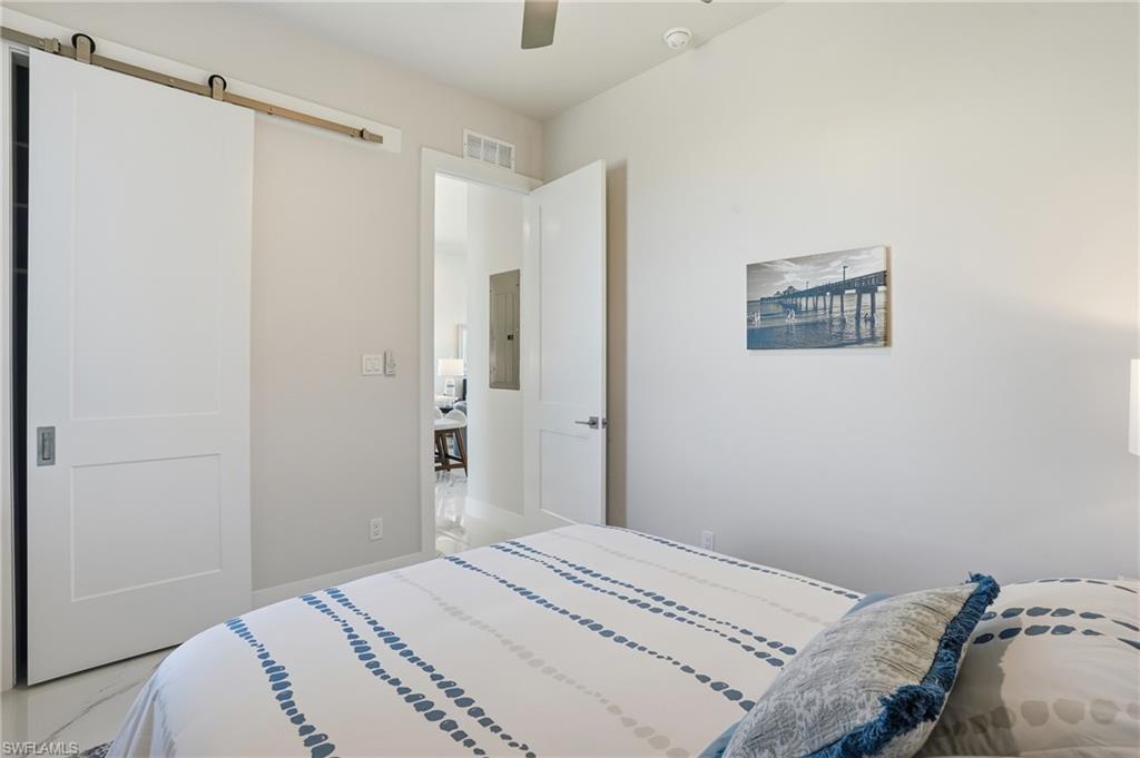 Bedroom featuring a barn door, ceiling fan, and electric panel - Virtually Edited Image