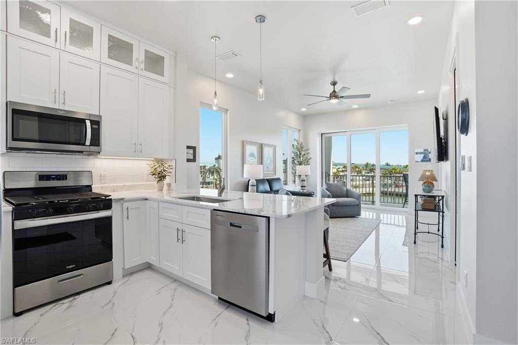 Kitchen featuring appliances with stainless steel finishes, white cabinets, light stone countertops, tasteful backsplash, and hanging light fixtures - Virtually Edited Image