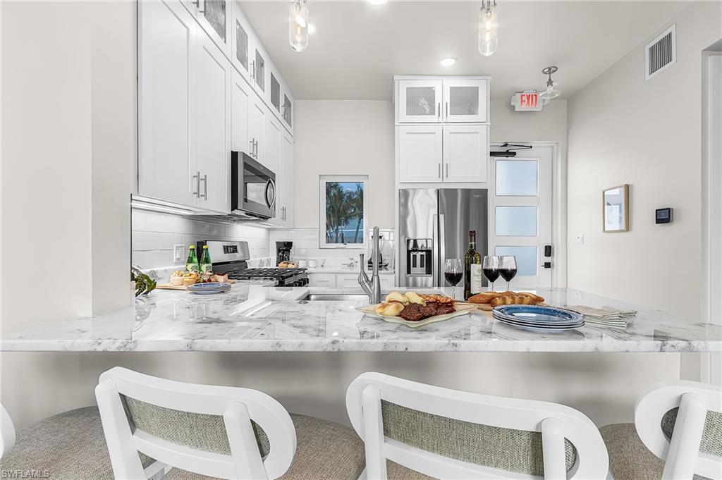 Kitchen featuring white shaker cabinetry, stainless steel appliances, a white subway tile backsplash, and a large island with a light-toned, veined countertop - Virtually Edited Image