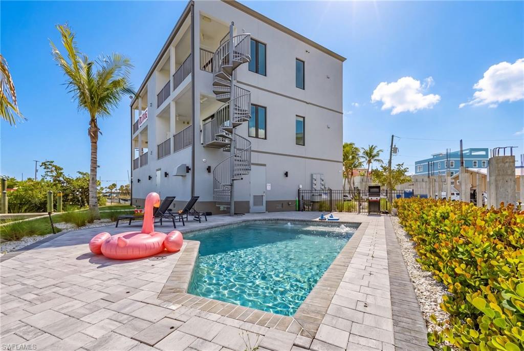 Multi-story property featuring a ground-level swimming pool with integrated spa jets, surrounded by a paver patio - Virtually Edited Image