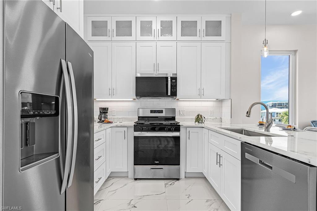 Contemporary kitchen featuring white cabinetry, stainless steel appliances, and white marble-look flooring - Virtually Edited Image