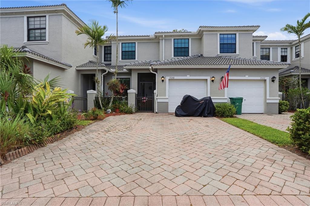 Gray stucco exterior featuring a two-car garage with white doors, a paver driveway, and a fenced front entry