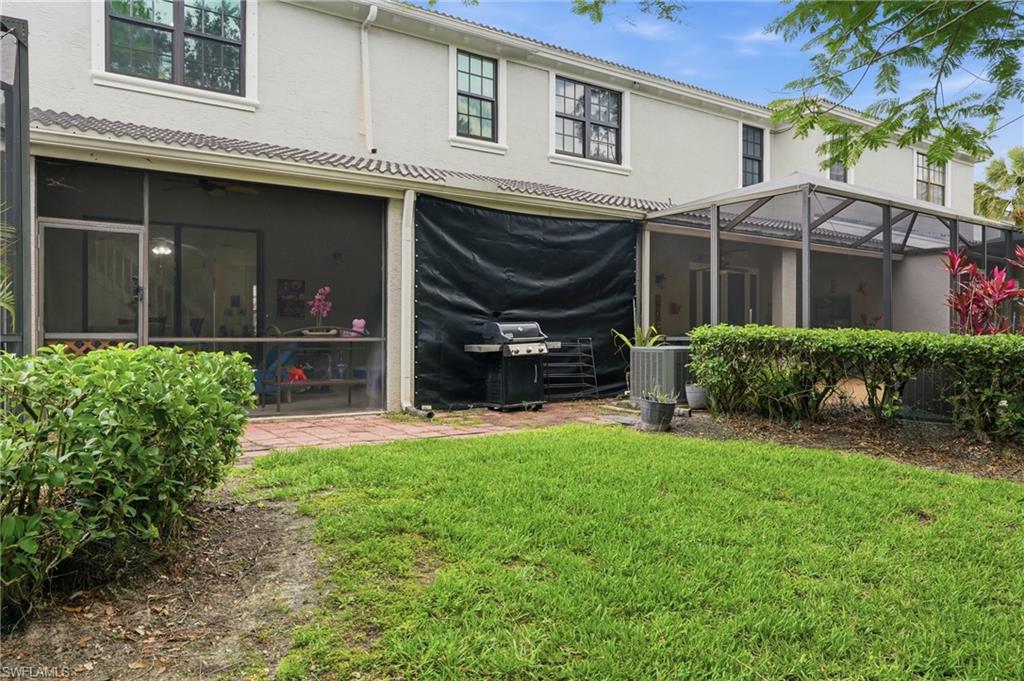 Rear exterior featuring a screened-in patio, an additional screened enclosure, a brick paver patio, and a grass lawn with shrubbery