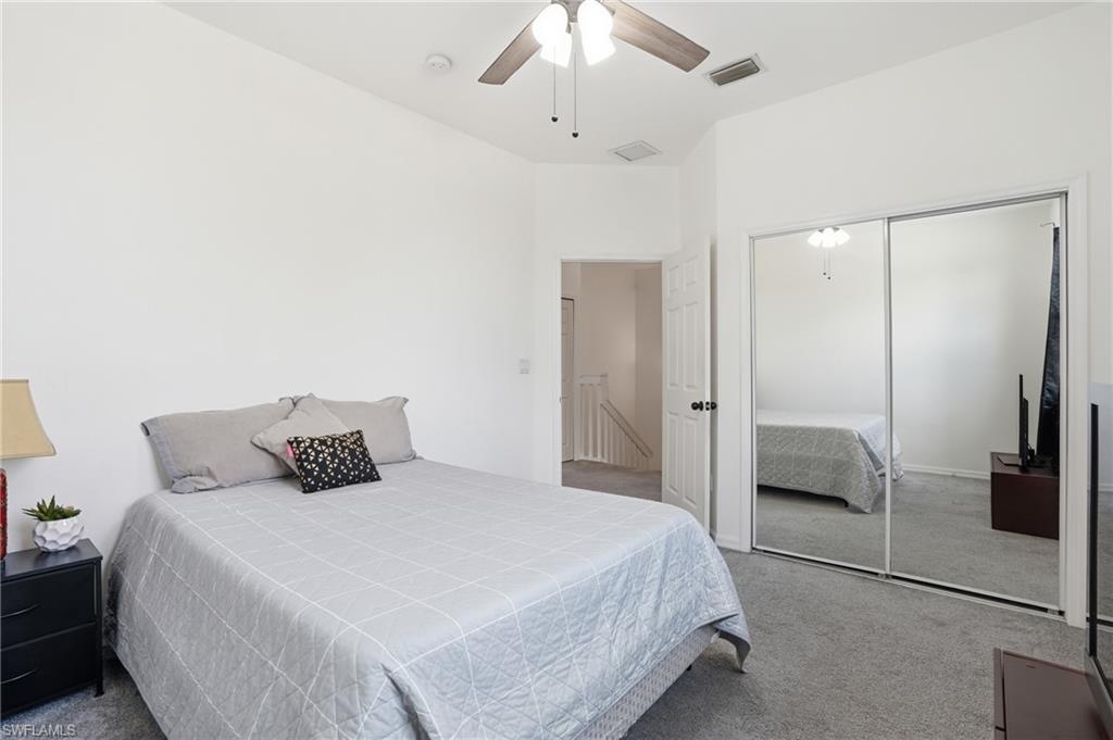 Carpeted bedroom featuring a mirrored closet, ceiling fan, and vaulted ceiling