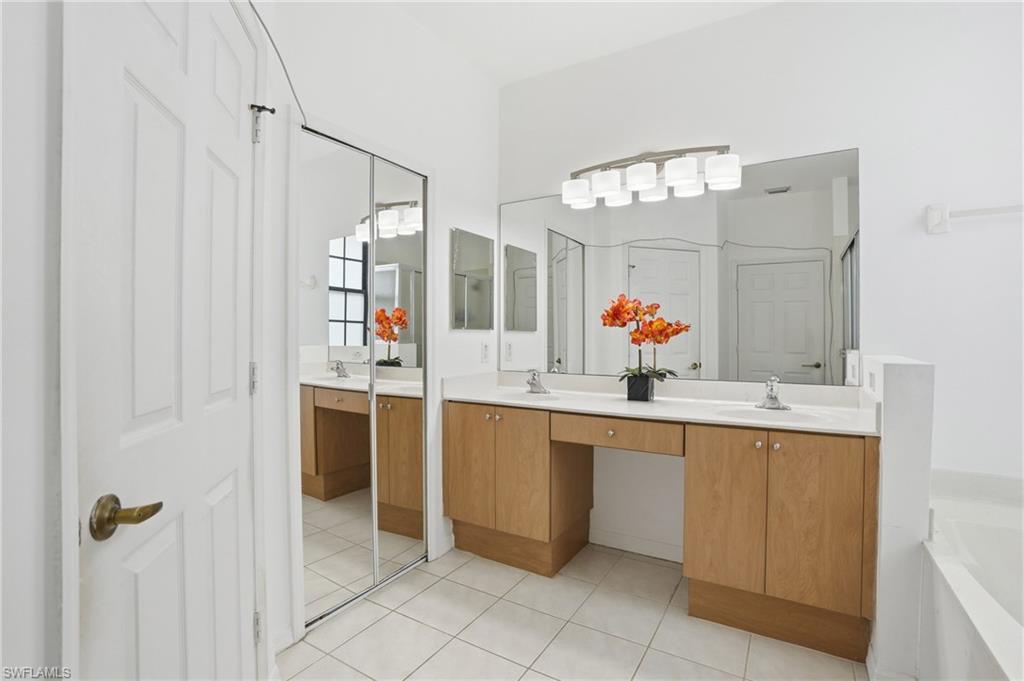 Bathroom featuring a double vanity with light wood cabinetry and white countertops, dual undermount sinks, and a built-in makeup vanity