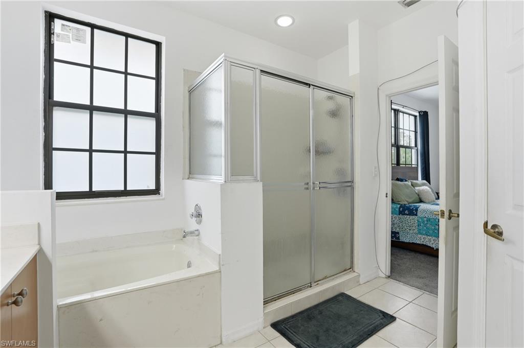 Bathroom featuring a built-in tub, a frosted glass shower enclosure with sliding doors, a black grid window, and recessed lighting
