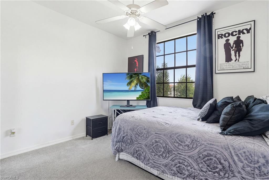 Carpeted interior space featuring a large window with gridded panes, a ceiling fan with integrated lighting, and white wall finishes