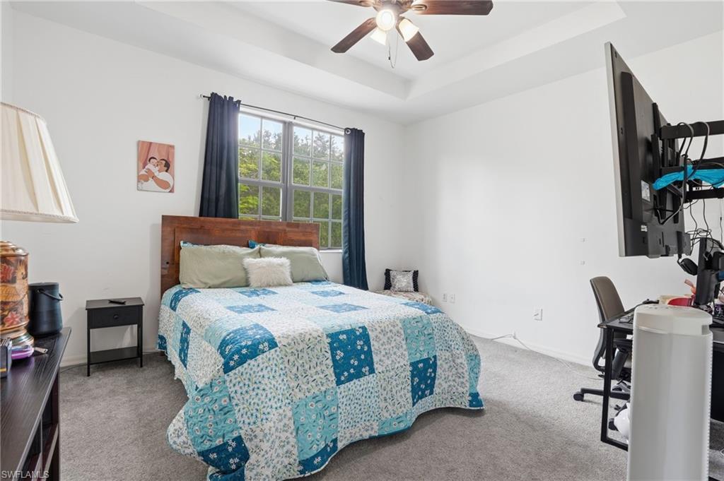 Recessed tray ceiling with a ceiling fan, window with exterior views, and neutral wall paint