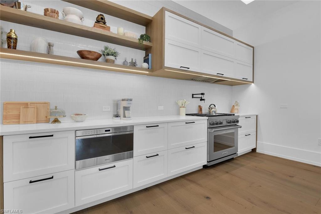 Bar featuring appliances with stainless steel finishes, backsplash, wood finished floors, and baseboards