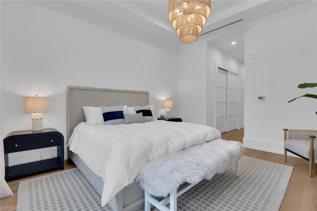 Bedroom featuring wood finished floors, a raised ceiling, baseboards, a closet, and a chandelier