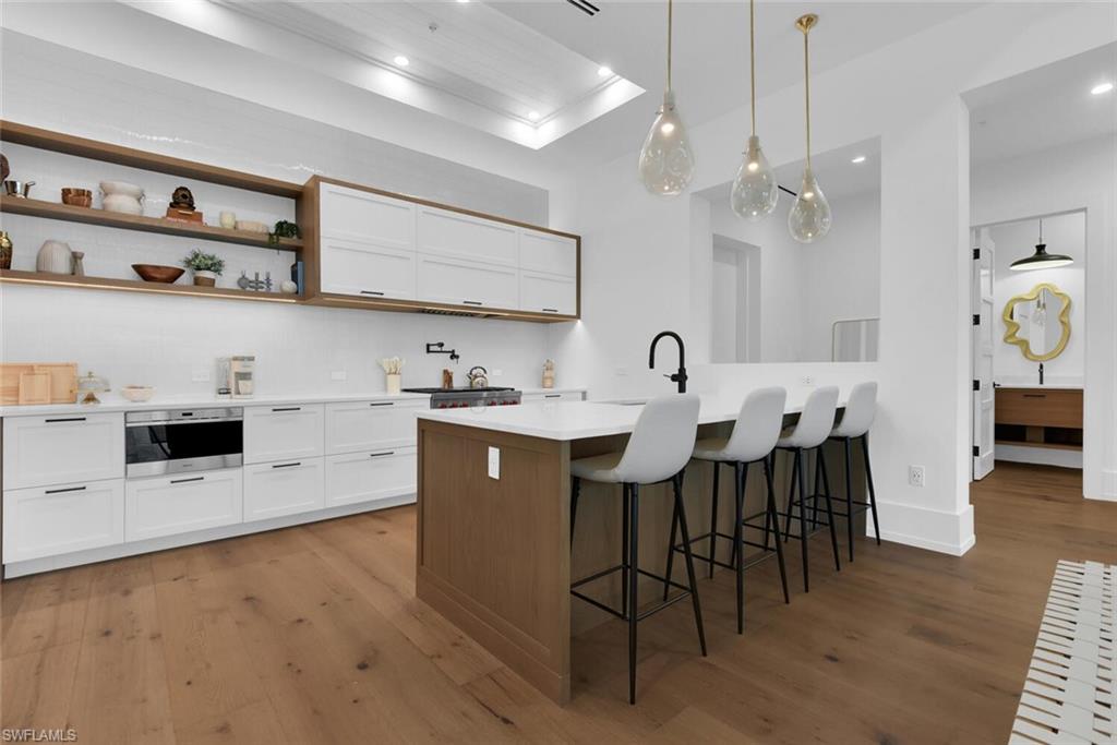 Kitchen with wood finished floors, white cabinets, a breakfast bar, light countertops, and a peninsula