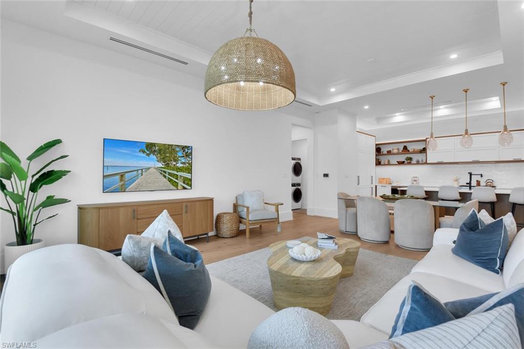 Living room with stacked washer / dryer, a tray ceiling, light wood finished floors, and recessed lighting