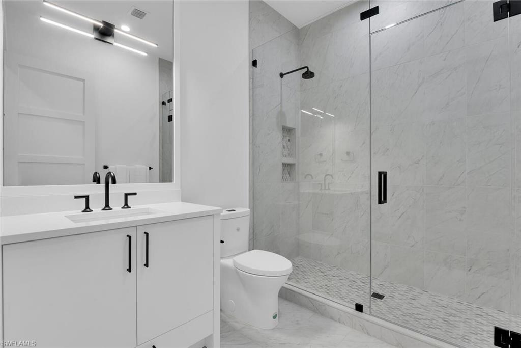 Full bath with a marble finish shower, marble look tile flooring, toilet, and vanity