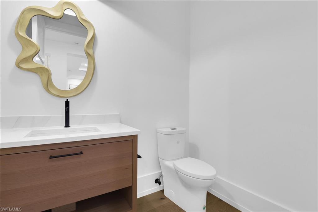 Bathroom with toilet, vanity, wood finished floors, and baseboards