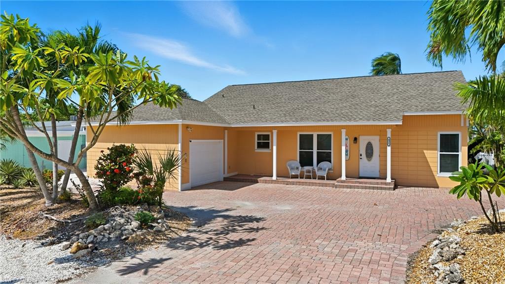 View of front of property with pavered driveway, an attached garage, and covered porch- Virtually Edited Image