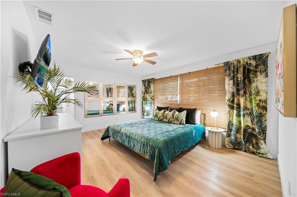 Spacious bedroom featuring wood-finish flooring, a ceiling fan with integrated lighting, and a wall of integrated mirrors