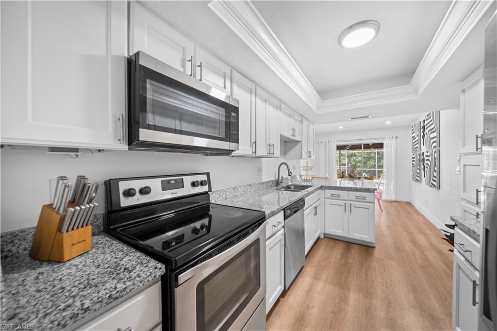 Bright kitchen featuring white cabinetry, stone countertops, stainless steel appliances, wood-finish flooring, and crown molding