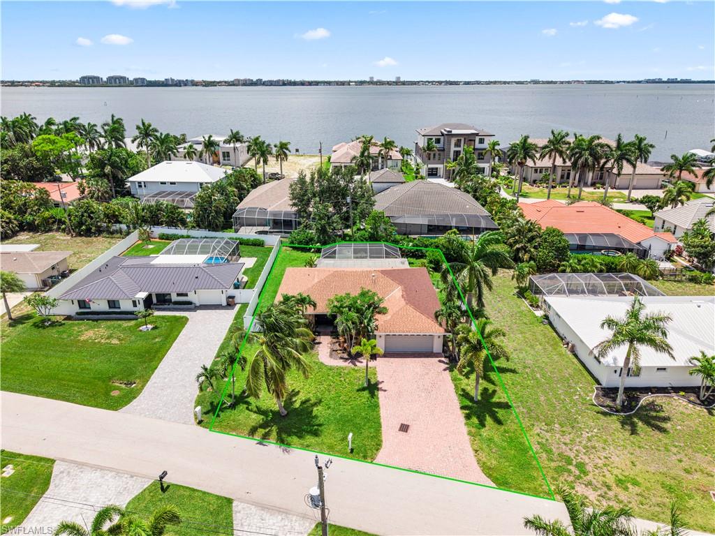 Aerial perspective showcasing a waterfront property with a red tile roof and a paver driveway