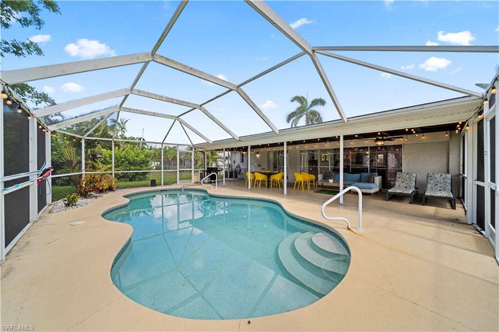 Screen-enclosed pool area featuring a freeform pool with integrated steps, a surrounding concrete deck, and a covered patio