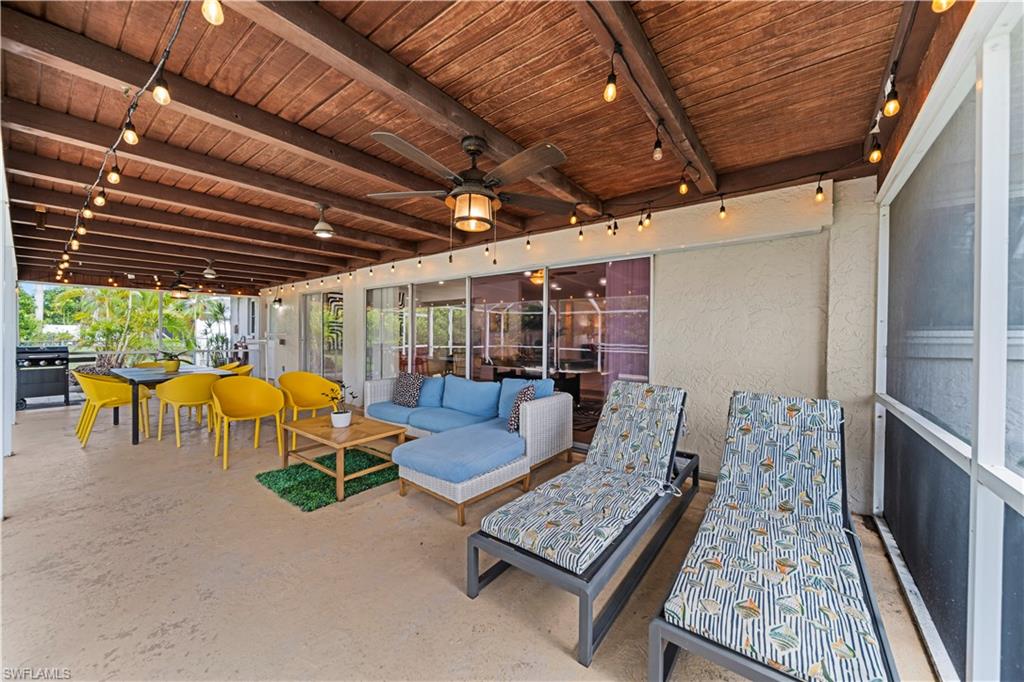 Expansive covered patio featuring a wood-plank ceiling with exposed beams, string lighting, and ceiling fans