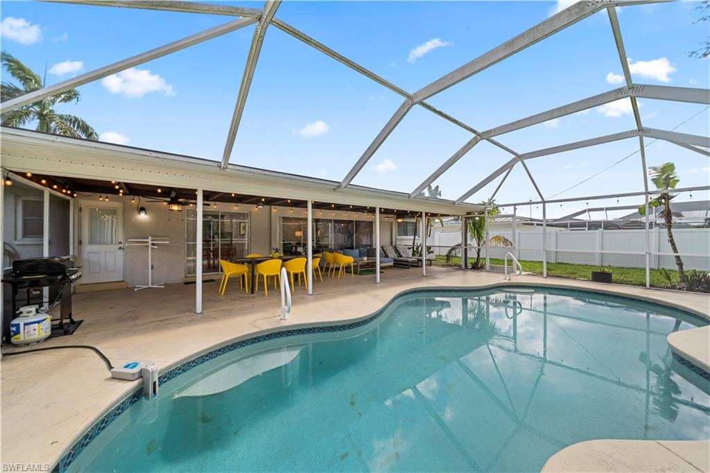 Screen-enclosed pool area featuring a freeform swimming pool, extensive concrete patio, covered patio, and a white privacy fence