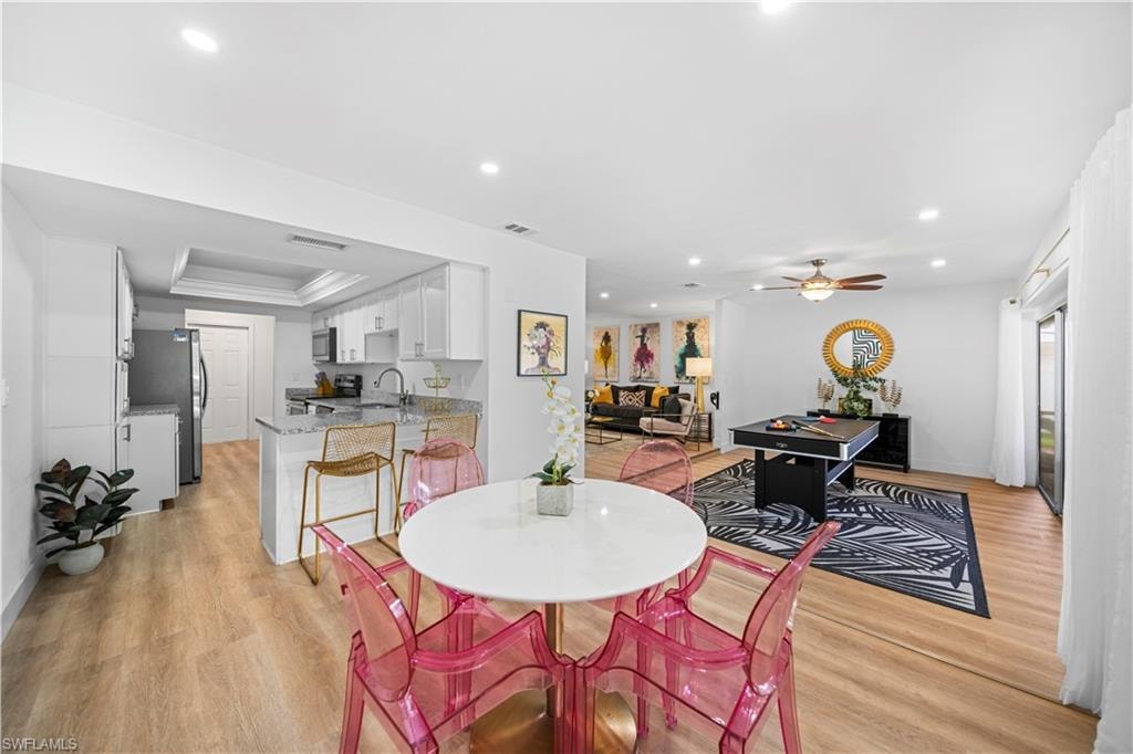 Open-concept living area with wood-finish flooring, recessed lighting, and a modern kitchen featuring white cabinetry and stainless steel appliances