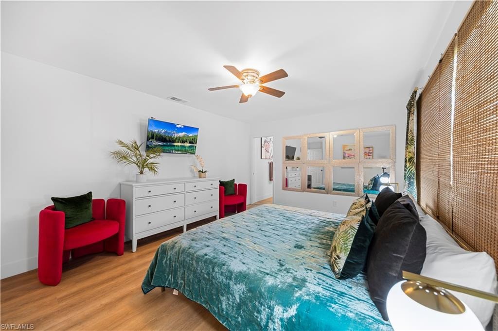 Spacious bedroom featuring wood-finish flooring, a ceiling fan, and window treatments