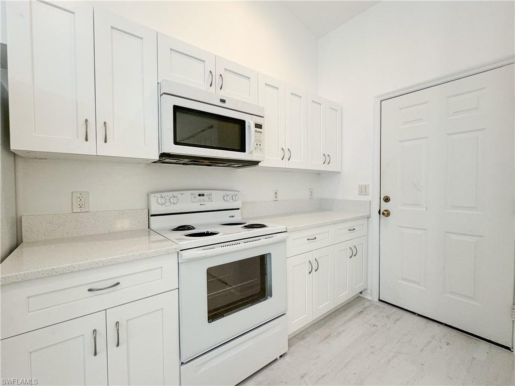 Kitchen featuring light stone countertops, white appliances, and white cabinets