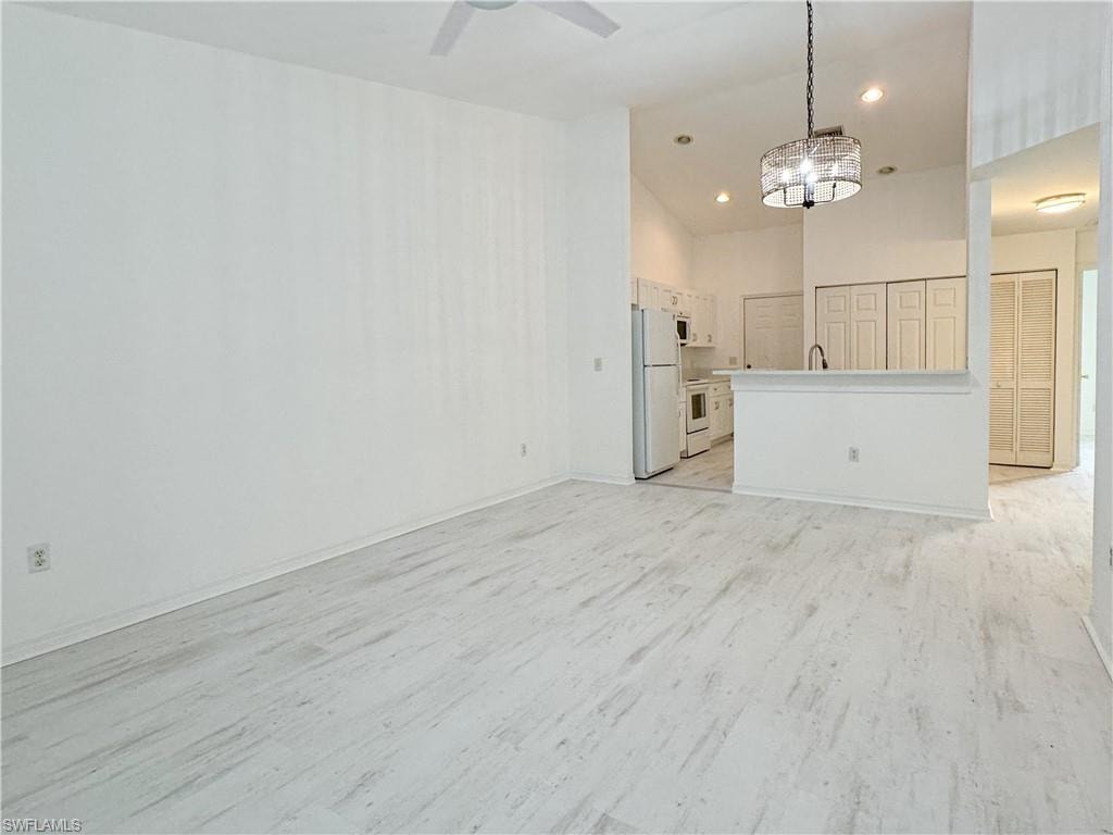 Unfurnished living room with sink, light wood-type flooring, high vaulted ceiling, and ceiling fan with notable chandelier