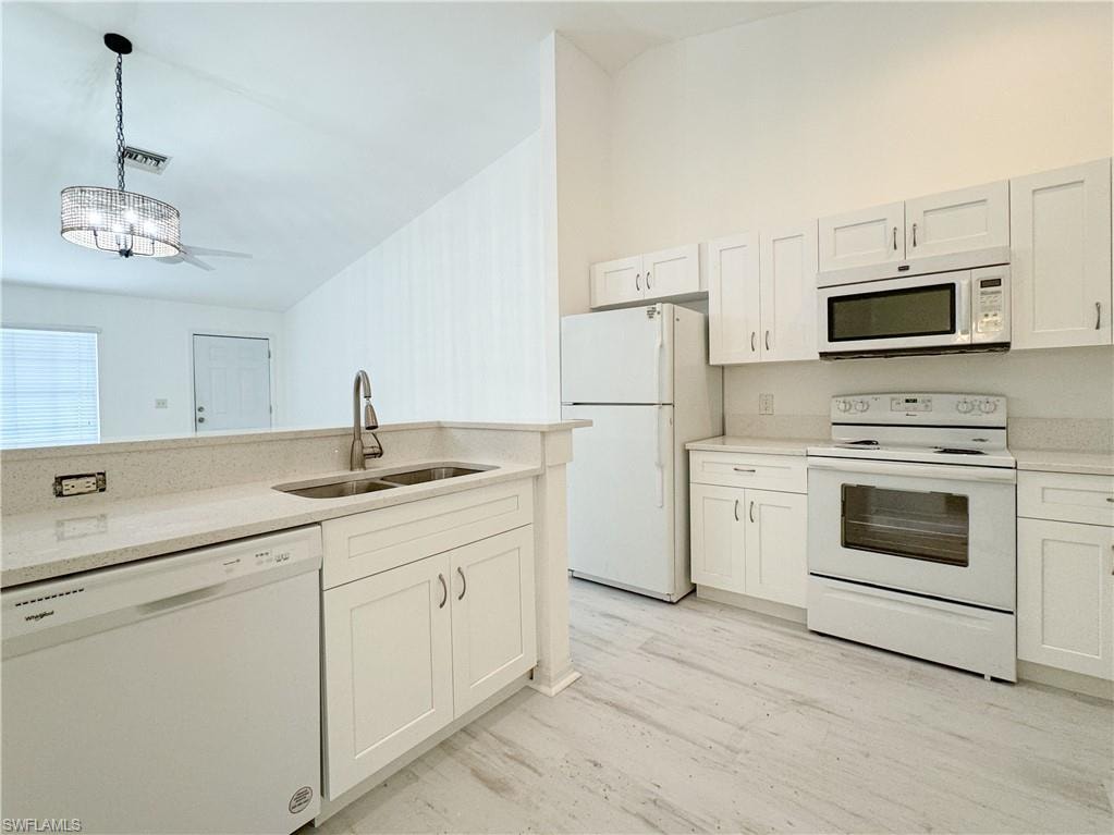 Kitchen with light wood-type flooring, pendant lighting, white cabinetry, sink, and white appliances