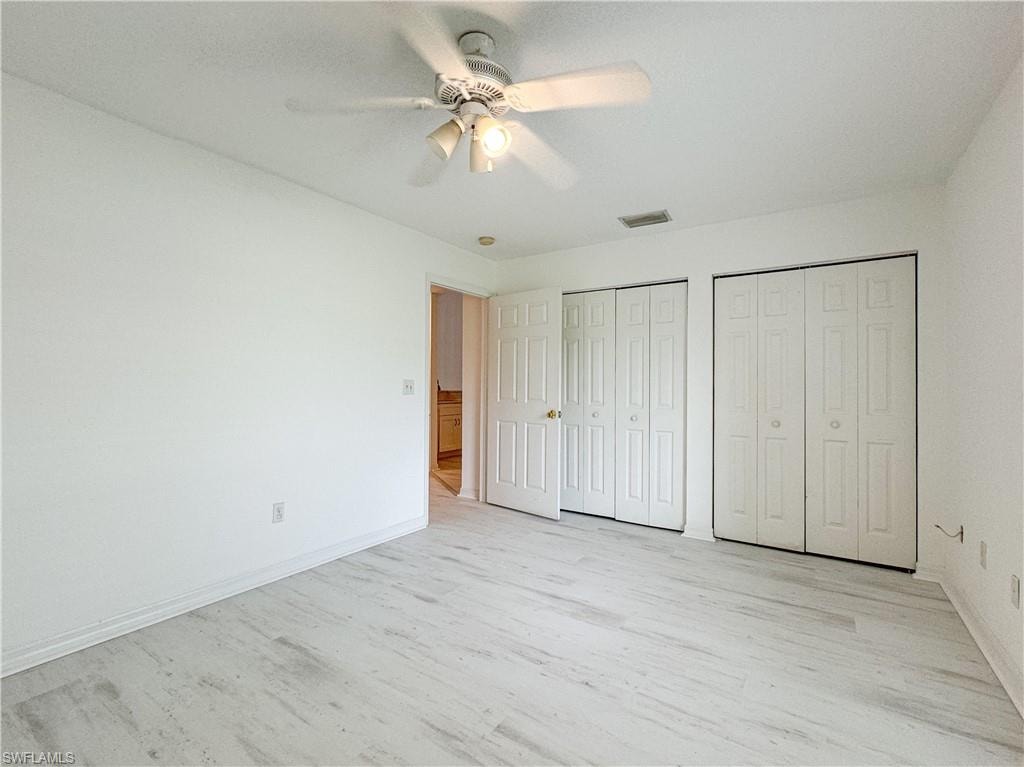 Unfurnished bedroom featuring light hardwood / wood-style flooring, ceiling fan, and multiple closets