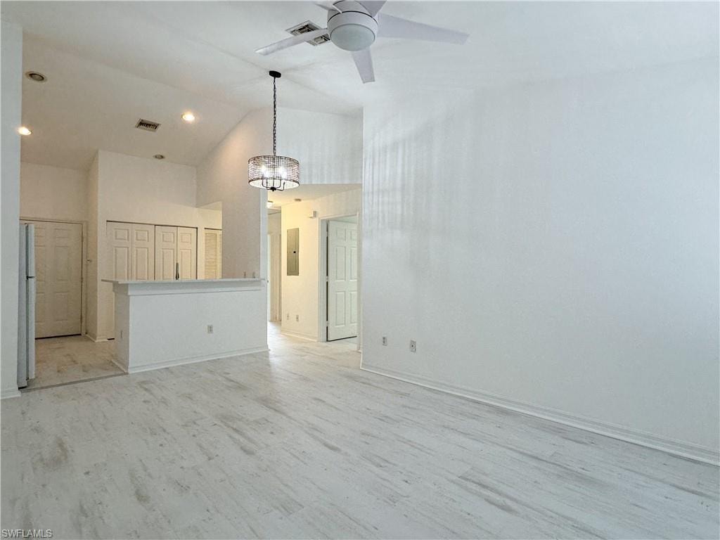 Unfurnished living room featuring high vaulted ceiling, light hardwood / wood-style flooring, ceiling fan with notable chandelier, and electric panel