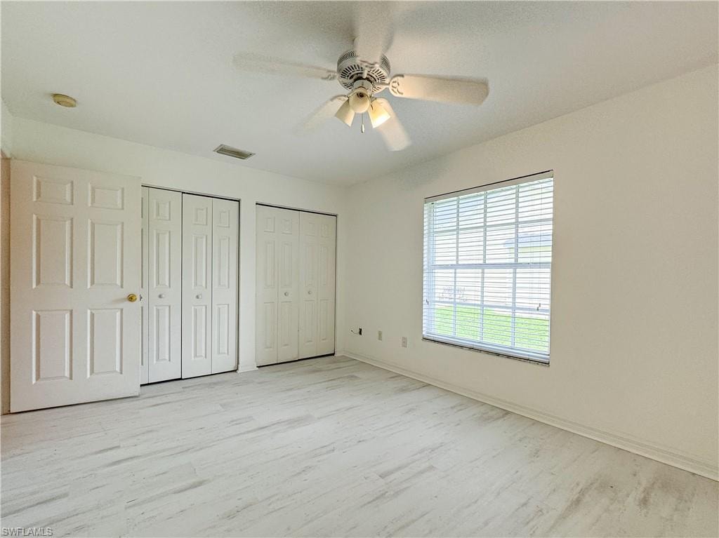Unfurnished bedroom featuring ceiling fan, light wood-type flooring, and multiple closets