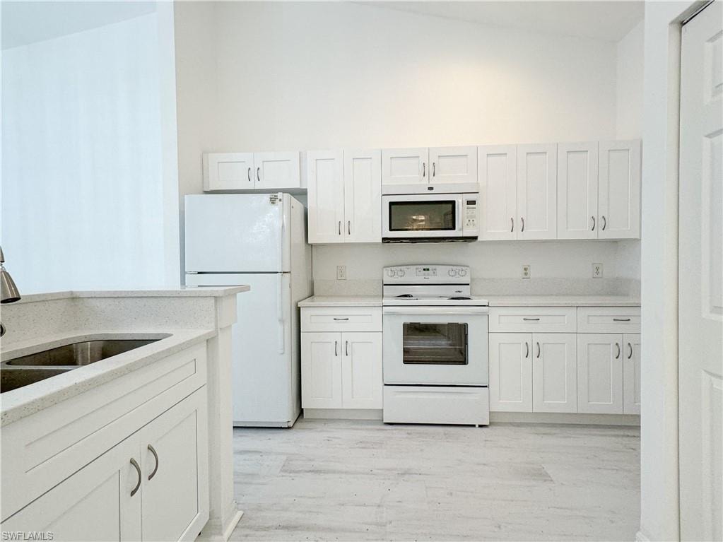 Kitchen with sink, light wood-type flooring, white appliances, white cabinets, and lofted ceiling