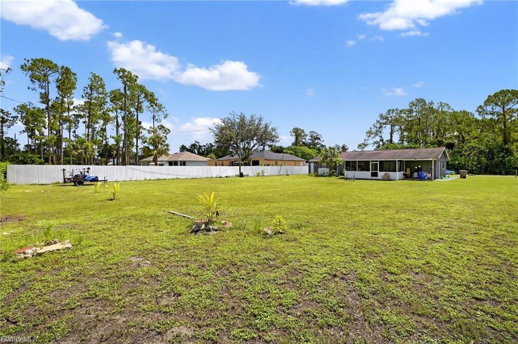 Expansive grass lawn featuring a white privacy fence and mature pine trees