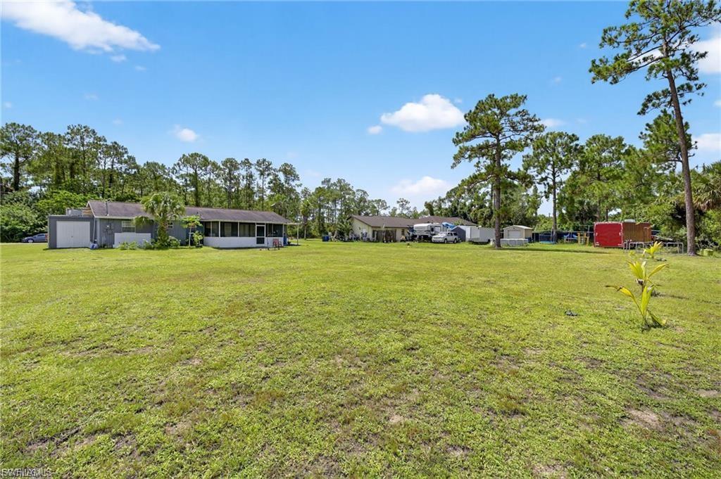 Expansive grassy yard with a distant single-story structure featuring a screened-in porch and an attached garage