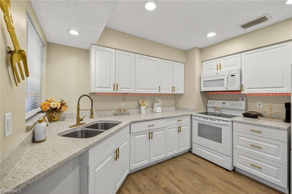 Kitchen featuring white cabinetry with gold-toned hardware, light-toned countertops, and wood-finish flooring