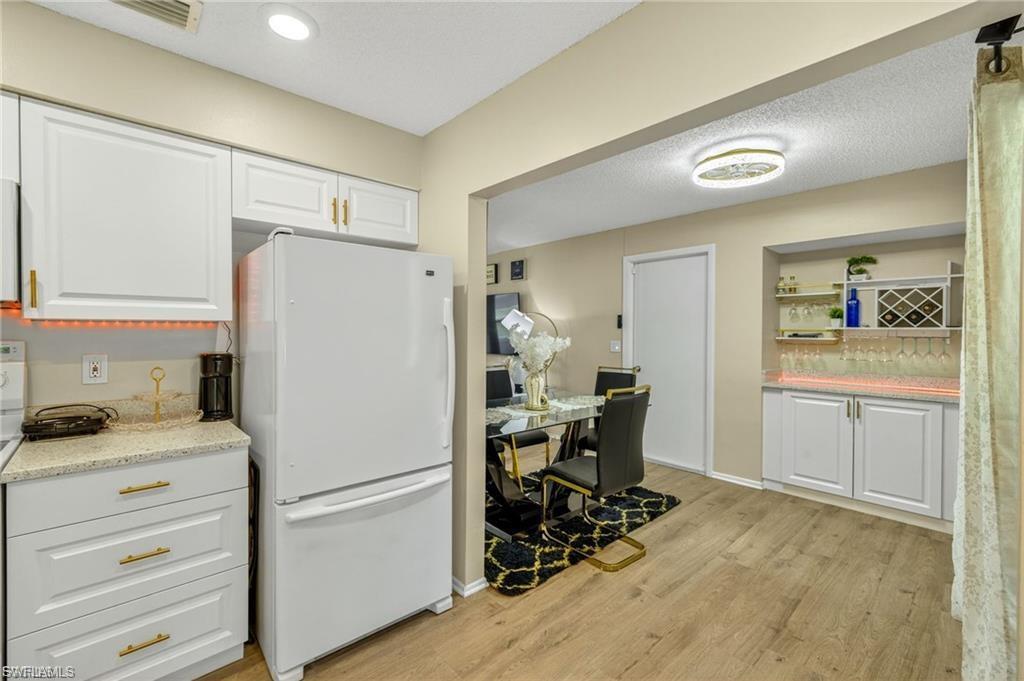 Kitchen and dining area featuring wood-finish flooring, white cabinetry with gold-tone hardware, granite-style countertops, and recessed lighting