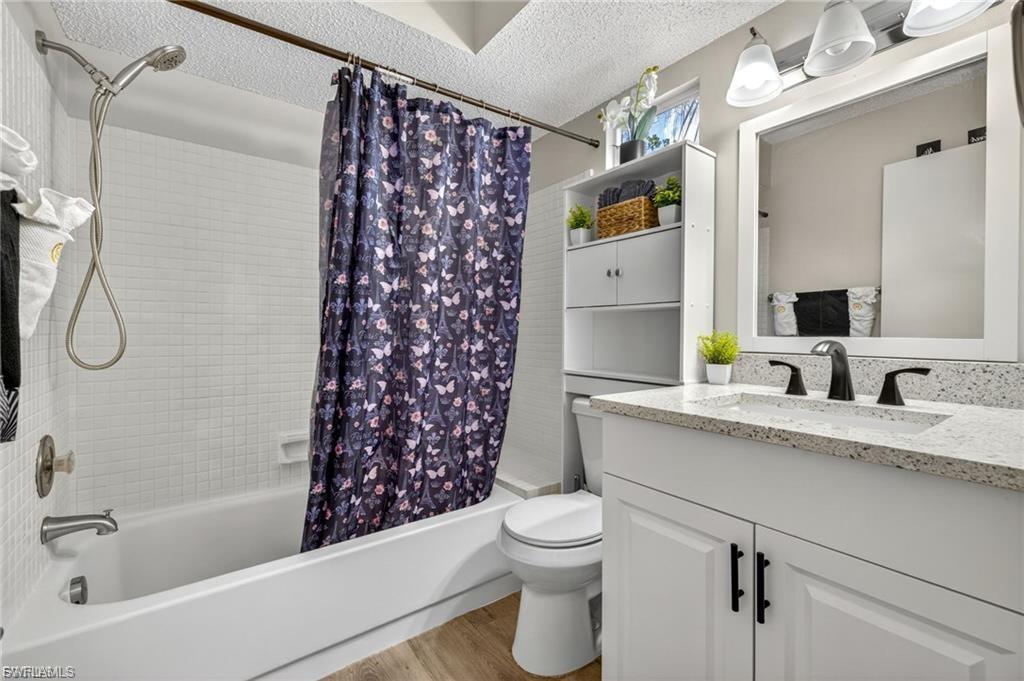 Bathroom featuring a tub/shower combination with white subway tile surround, a white vanity with a speckled countertop, a rectangular mirror, and wood-finish flooring