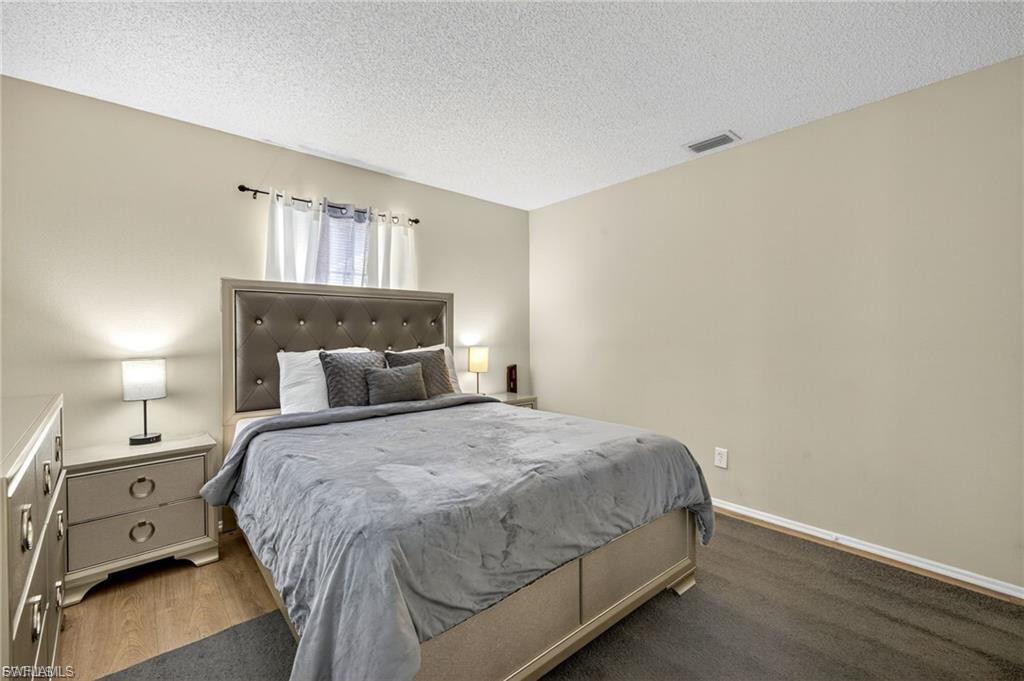 Bedroom featuring light neutral wall paint, a window with curtains, wood-finish flooring, and a textured ceiling
