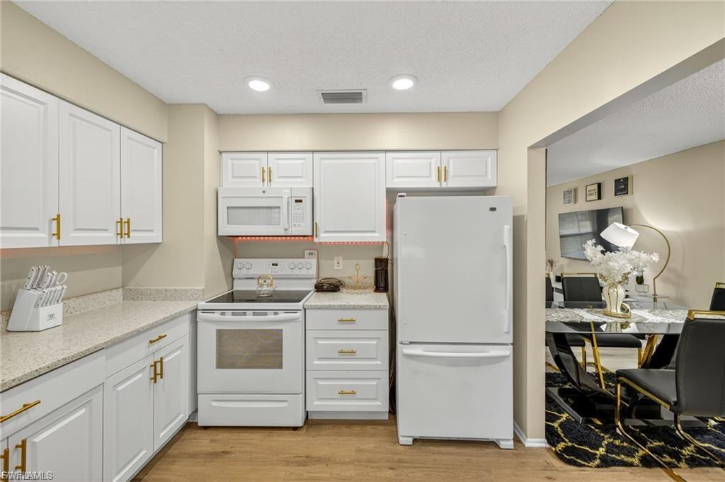 Kitchen featuring white cabinetry with gold-toned hardware, light-toned countertops, wood-finish flooring, a white electric range, and a white refrigerator