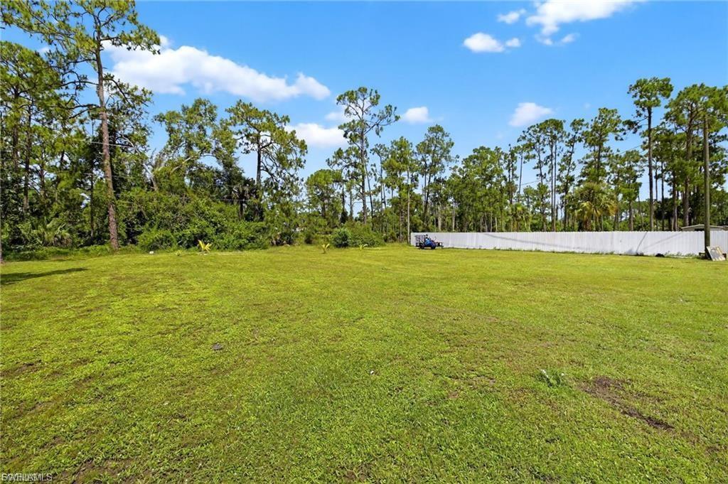 Expansive green lawn surrounded by mature trees, featuring a white privacy fence along the perimeter