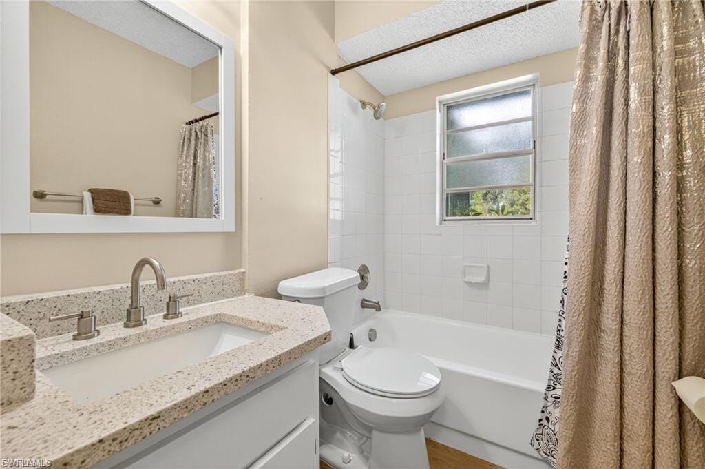 Bathroom featuring a white vanity with a speckled countertop, a rectangular sink with a brushed nickel faucet, a framed mirror, white tiled shower surround, and a window for natural light