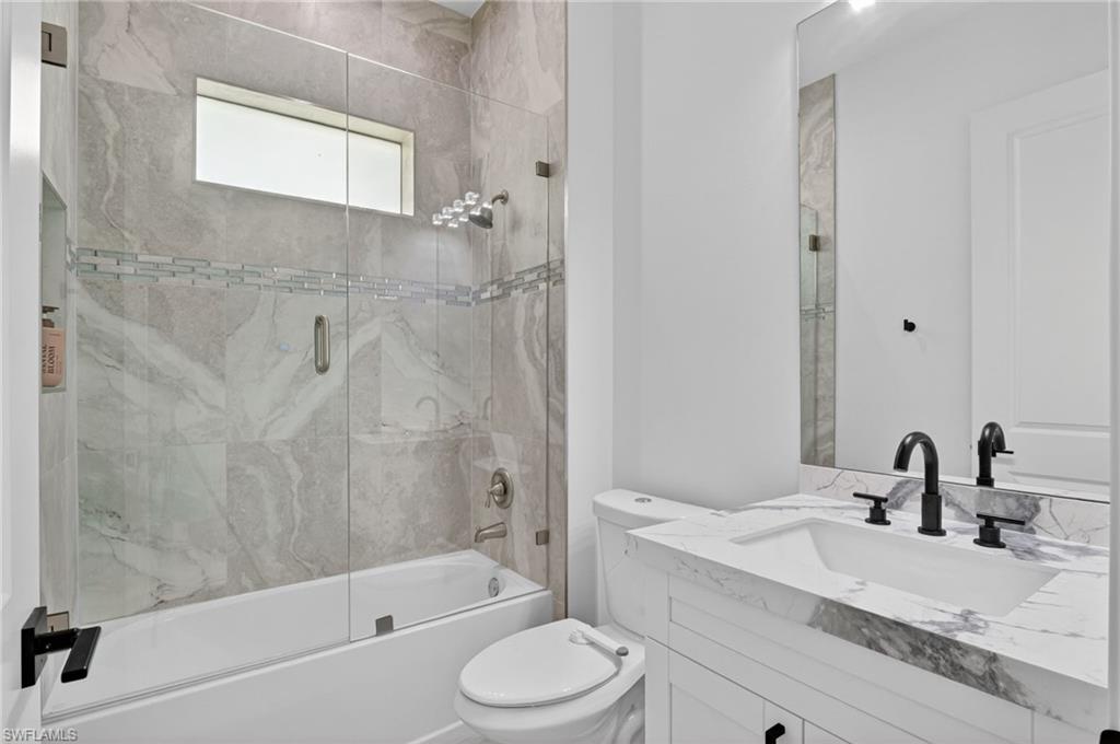 Full bathroom featuring a tub-shower combination with floor-to-ceiling tile surround and glass enclosure