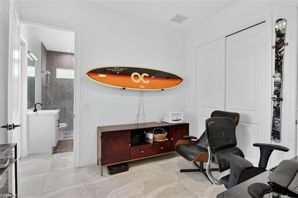 Bright interior space featuring light-toned tile flooring, white walls, and a doorway leading to an additional bathroom with a vanity and dark-tiled shower