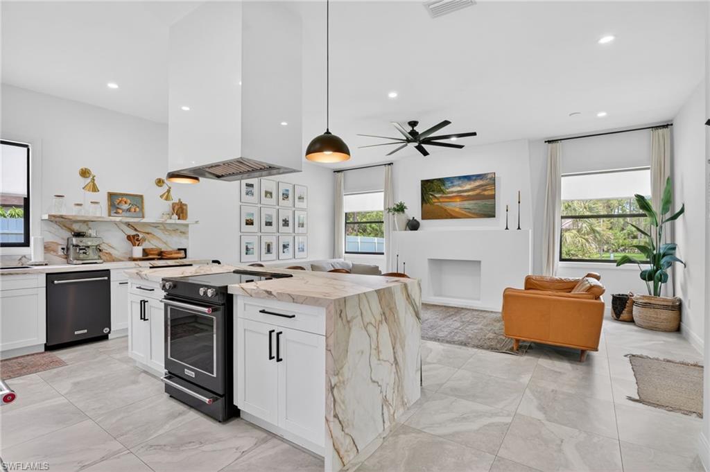 Open-concept living area featuring a kitchen island with stone waterfall countertops, black appliances, a modern range hood, and light tile flooring