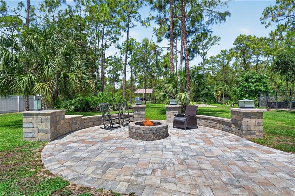 Paver patio featuring a built-in stone fire pit, stone-block retaining wall, and integrated pillar lighting