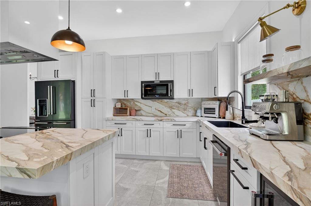 Modern kitchen featuring an expansive island with a waterfall edge, white shaker cabinetry, gold-veined countertops, built-in appliances, and a black sink with a gooseneck faucet